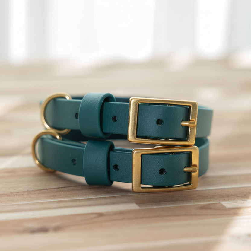 Two emerald Biothane dog collars with brass buckles on a wooden surface.