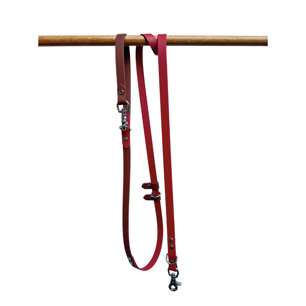 Red Biothane dog leash with metal clips on a wooden rod against a white background
