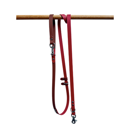 Red Biothane dog leash with metal clips on a wooden rod against a white background