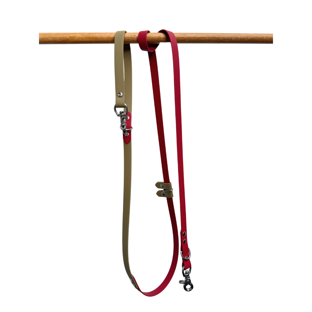 Red and beige dog leash with clips on a wooden rod against a white background
